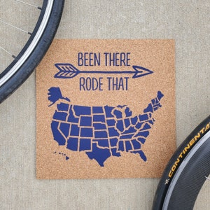 May include: A corkboard with a blue outline of the United States of America, with each state outlined. The text "Been There Rode That" is above the map with a blue arrow pointing to the right.