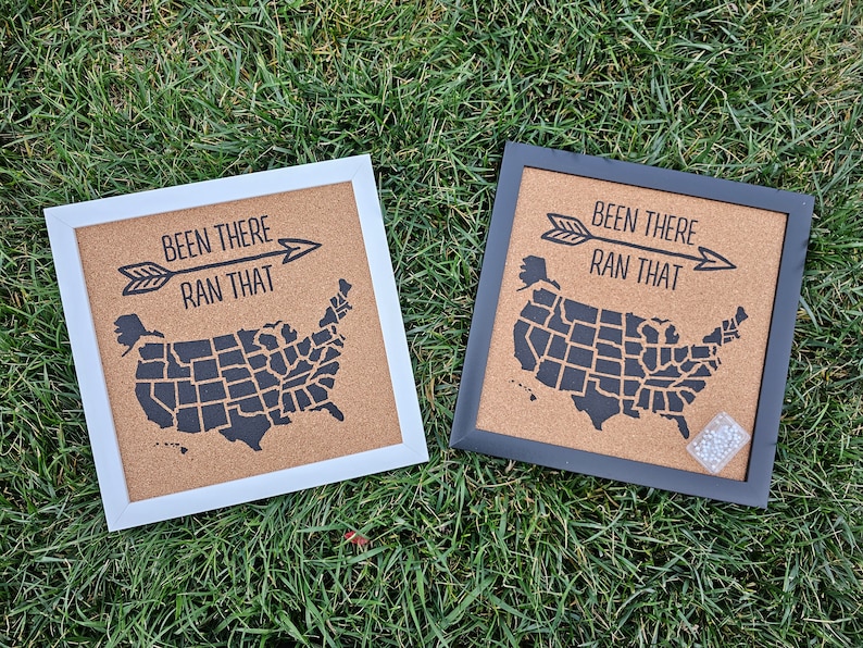 K&ouml;nnte beinhalten: Zwei Korktafeln mit schwarzem Rahmen und wei&szlig;em Hintergrund. Die Schilder zeigen eine Karte der Vereinigten Staaten mit dem Text "Been There Ran That" und einem schwarzen Pfeil.