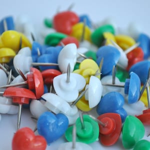 May include: A pile of colorful heart-shaped push pins. The pins are in various colors, including red, blue, yellow, green, and white.
