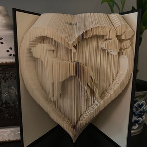 May include: A book with pages folded into a heart shape, creating a 3D design of two dogs inside the heart.