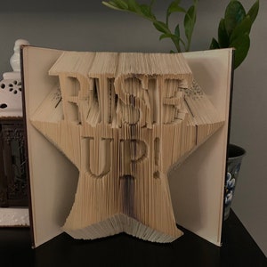 May include: A book folded into the shape of a star with the words "Haste Up!" formed by the pages.