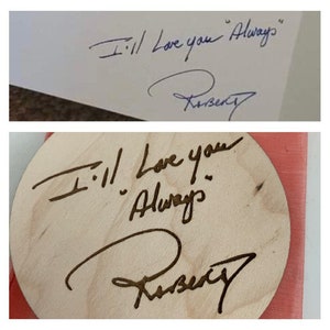 May include: A close-up of a wooden circle with the words "I'll love you Always" and a signature. The circle is on a pink surface.