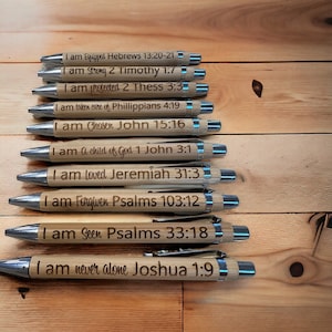 May include: Ten wooden pens with silver accents. Each pen has a different inspirational quote and bible verse engraved on it. The quotes include "I am Equipped", "I am Strong", "I am Protected", "I am Taken Care Of", "I am Chosen", "I am a Child of God", "I am Loved", "I am Forgiven", "I am Seen", and "I am Never Alone".
