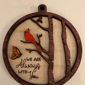 May include: A wooden ornament with a red cardinal perched on a branch, a butterfly, and the text "We are Always With You".