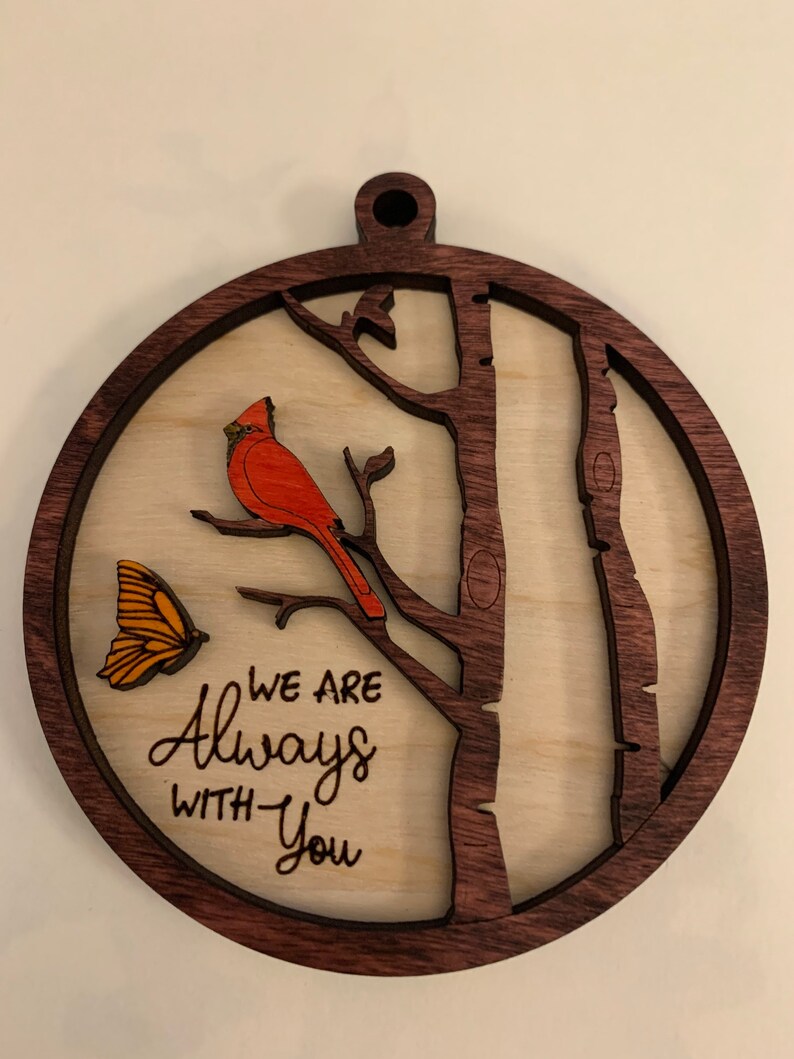 May include: A wooden ornament with a red cardinal perched on a branch, a butterfly, and the text "We are Always With You".