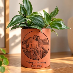 Op de afbeelding: Een cilindervormige, terracotta-kleurige plantenpot met een cirkelvormig, zwart gegraveerd portret van een gezin van vier. Onder de afbeelding staat de tekst "Harper Family" en "09.11.2025". Een Tradescantia zebrina plant groeit eruit.