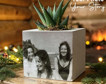 May include: A square concrete planter featuring a black and white photograph of three people printed on the front side. A green succulent plant grows from the top of the planter. The text Your Photo Your Story is visible above.