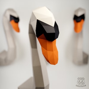 May include: Three origami swans made of paper. The swans are white with black and orange accents. The swans are arranged in a row with the middle swan in focus.
