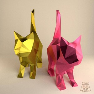 K&ouml;nnte beinhalten: Zwei Origami-Katzen, eine gelbe und eine rosa, stehen auf einer hellbeigen Oberfl&auml;che. Die Katzen sind aus Papier und haben ein geometrisches Design.