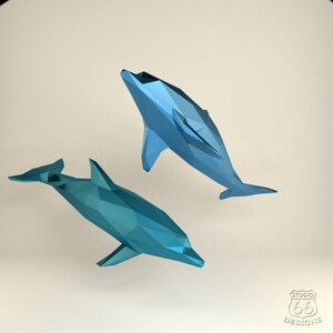 Może przedstawiać: Dwa niebieskie origami w kształcie delfin&oacute;w, jeden zwr&oacute;cony w lewo, a drugi w prawo, na białym tle.