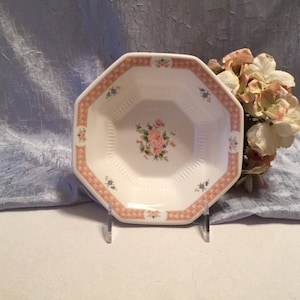 May include: A white octagonal ceramic bowl with a pink and blue floral design. The bowl has a scalloped edge and a raised rim.