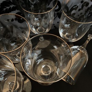 Puede incluir: Seis copas de vino de vidrio transparente con borde dorado. Las copas est&aacute;n apiladas unas sobre otras.
