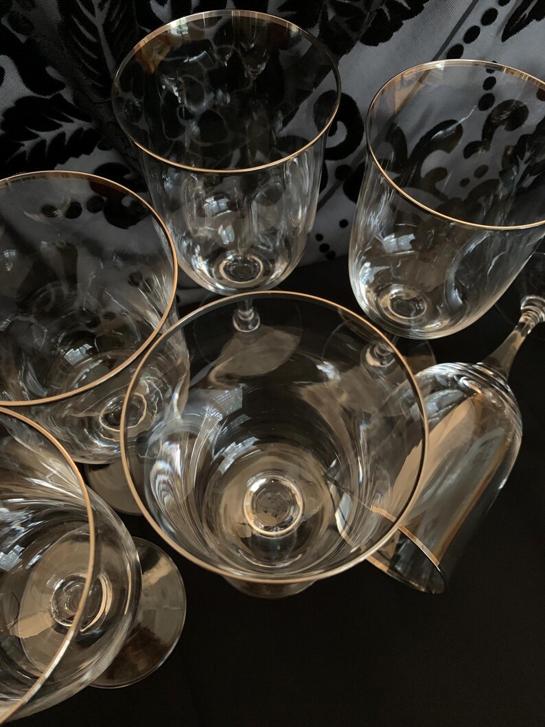 Puede incluir: Seis copas de vino de vidrio transparente con borde dorado. Las copas est&aacute;n apiladas unas sobre otras.