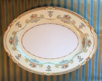 May include: An oval serving platter with a white background and a gold rim. The platter is decorated with a floral pattern in shades of pink, blue, and green.