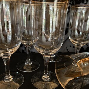 Puede incluir: Juego de seis copas de vino de vidrio transparente con borde dorado. Las copas est&aacute;n dispuestas en c&iacute;rculo sobre una superficie negra.