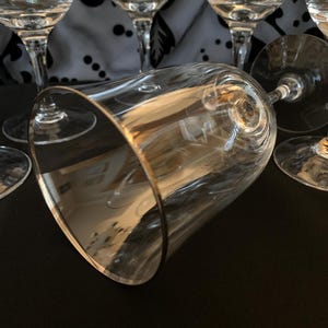Puede incluir: Un juego de seis copas de vino de vidrio transparente con bordes dorados. Las copas est&aacute;n dispuestas en grupo, con una copa en primer plano y las dem&aacute;s en el fondo.