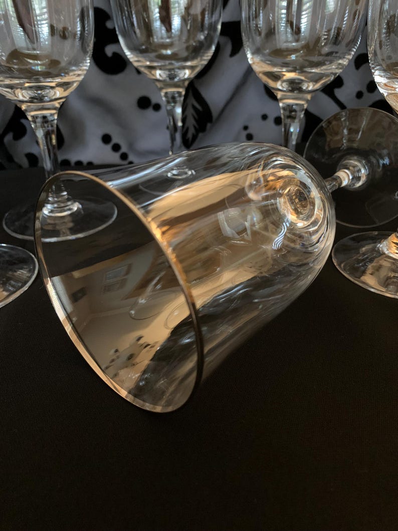 Puede incluir: Un juego de seis copas de vino de vidrio transparente con bordes dorados. Las copas est&aacute;n dispuestas en grupo, con una copa en primer plano y las dem&aacute;s en el fondo.