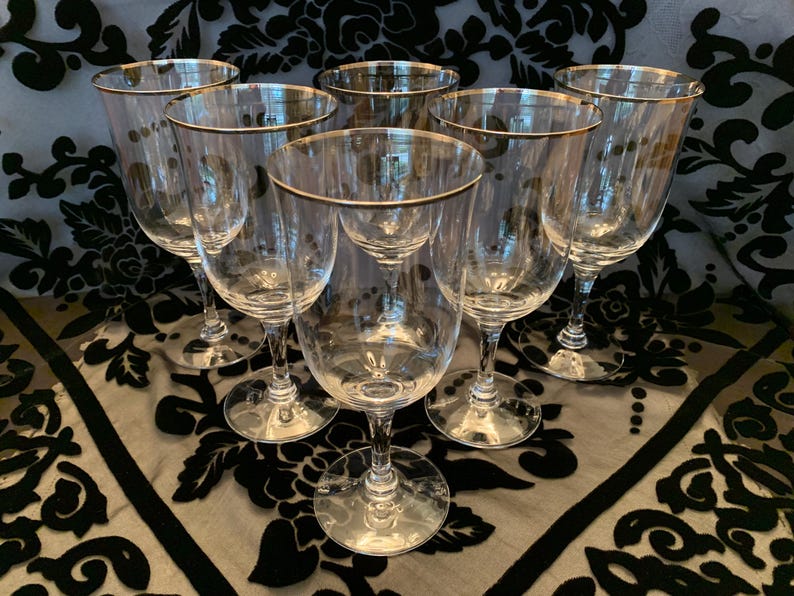 Puede incluir: Juego de seis copas de vidrio transparente con borde dorado. Las copas est&aacute;n dispuestas en c&iacute;rculo sobre una superficie con estampado blanco y negro.
