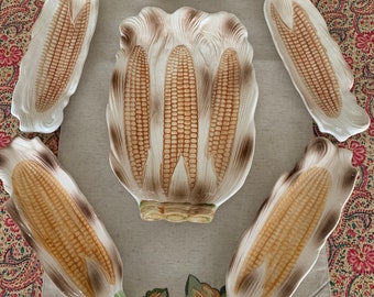 May include: Set of six ceramic corn on the cob serving dishes. The dishes are white with brown and yellow details. The dishes are shaped like corn on the cob and have a realistic design.