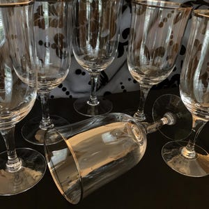 Puede incluir: Conjunto de seis copas de vino de vidrio transparente con borde dorado. Las copas est&aacute;n dispuestas en semic&iacute;rculo sobre una superficie negra.