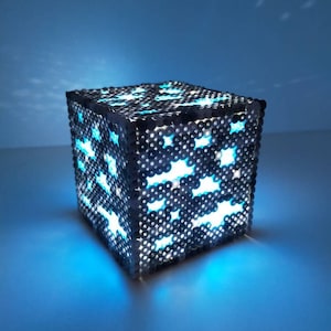 May include: A blue and gray cube-shaped night light made of beads, with a glowing blue light emanating from the inside.