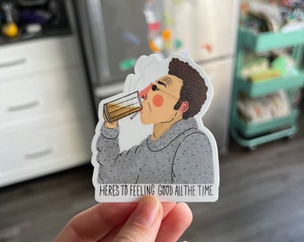 Può includere: Un adesivo con un'illustrazione a cartoni animati di un uomo che beve da una tazza. L'uomo indossa occhiali e un maglione grigio. L'adesivo include il testo "HERE'S TO FEELING GOOD ALL THE TIME".