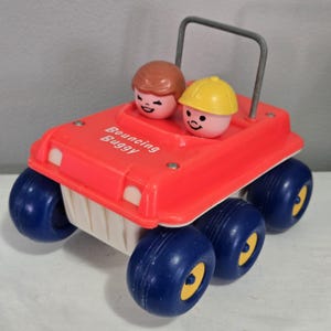 May include: A vintage red plastic toy car with blue wheels and a silver roll bar. The car has two smiling plastic figures inside. The text "Bouncing Buggy" is printed on the front of the car. The wheels have yellow centers.