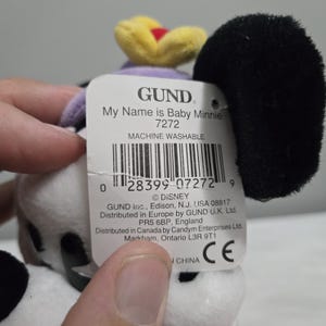 May include: A Baby Minnie plush toy with a black ear, a yellow and red flower, and a tag that reads "My Name is Baby Minnie 7272". The toy is white with black spots.