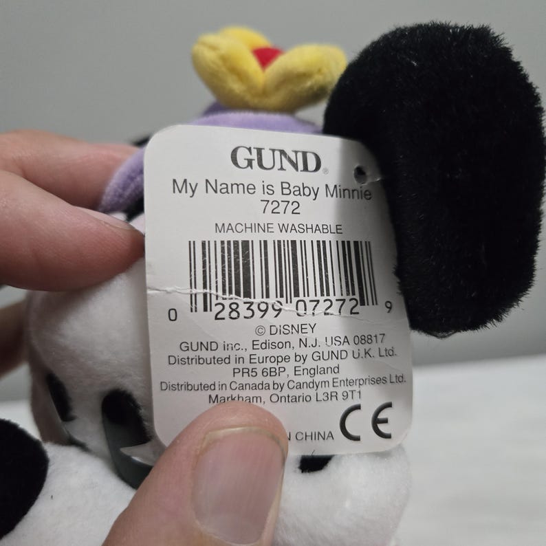 May include: A Baby Minnie plush toy with a black ear, a yellow and red flower, and a tag that reads "My Name is Baby Minnie 7272". The toy is white with black spots.