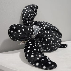 May include: A plush sea turtle toy in black with white polka dots. The turtle has a soft, textured body, flippers, and a head with a detailed face. The toy is designed to resemble a real sea turtle and is suitable for children.