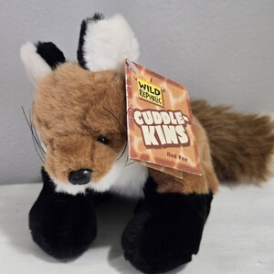 May include: A plush red fox toy with a brown body, white chest, and black paws. The fox has a fluffy tail and a tag that reads "Cuddle Kins Red Fox" from Wild Republic.