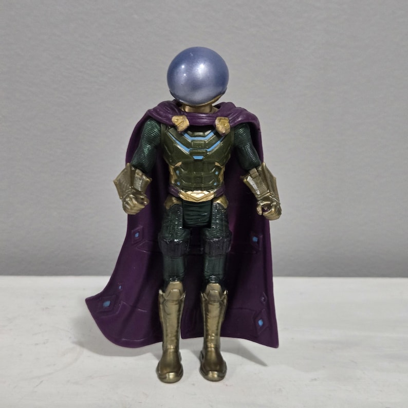 May include: A Mysterio action figure, featuring a metallic blue spherical helmet and a purple cape. The figure has a green and gold armored suit with gold boots and gauntlets. The cape has a diamond pattern.