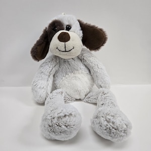 Può includere: Un giocattolo di peluche grigio e bianco a forma di cane con orecchie marroni. Il cane ha un viso sorridente con occhi neri e un naso marrone.