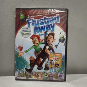 May include: DVD case for the animated movie Flushed Away, featuring the characters Roddy and Rita on a surfboard, with the text "Flushed Away" in large, bold letters. The case also features the text "From the creators of Shrek" and "Souris City".