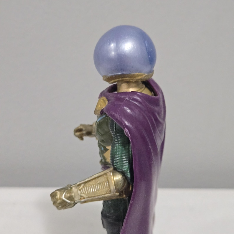 May include: A Mysterio action figure, featuring a metallic gold and green armored suit, a purple cape, and a blue, spherical helmet. The figure is posed in a dynamic stance, showcasing intricate details.