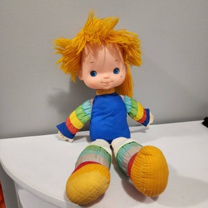 May include: A vintage Rainbow Brite doll with yellow yarn hair, a blue shirt, and rainbow striped sleeves and legs.
