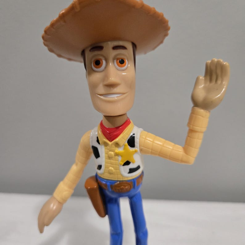 Pu&ograve; includere: Una figurina di plastica di Woody di Toy Story. Indossa il suo cappello da cowboy, il gilet e i jeans caratteristici. Sta salutando con la mano destra.