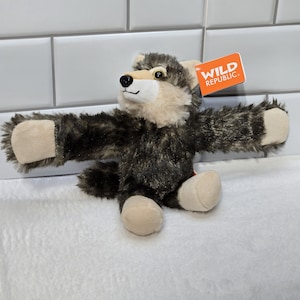 May include: A brown and gray plush wolf with a tan face and paws. The wolf is sitting with its arms outstretched. The wolf has a tag that says "WILD REPUBLIC" on it.