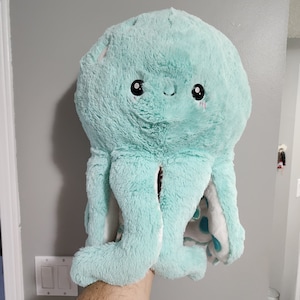 May include: A soft, plush, light blue octopus with white accents and black eyes. The octopus has a friendly expression and is made of a soft, cuddly material.