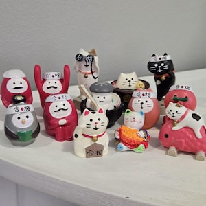 May include: A collection of 12 small, colorful figurines of cats and other animals. The figurines are made of ceramic and have a traditional Japanese design. Each figurine has the Japanese word "合格" written on it, which means "pass" or "success".