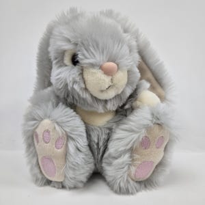 May include: A plush, gray bunny rabbit with long, floppy ears and a pink nose. The bunny has soft, fluffy fur and light pink paw pads. The bunny is sitting upright, with its paws in front.