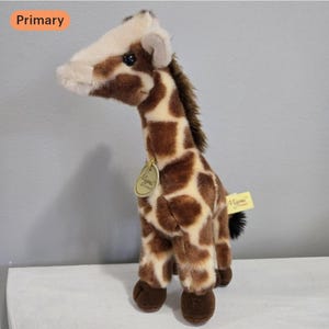 May include: A plush giraffe toy with a brown and cream spotted pattern. The giraffe has a light brown face and dark brown hooves. It has a tag that says "Mimi & Friends".
