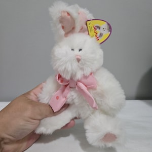 May include: A white plush bunny with pink polka dot accents on the ears and a pink bow. The bunny has a pink nose and blue eyes. A yellow tag is attached to the ear.