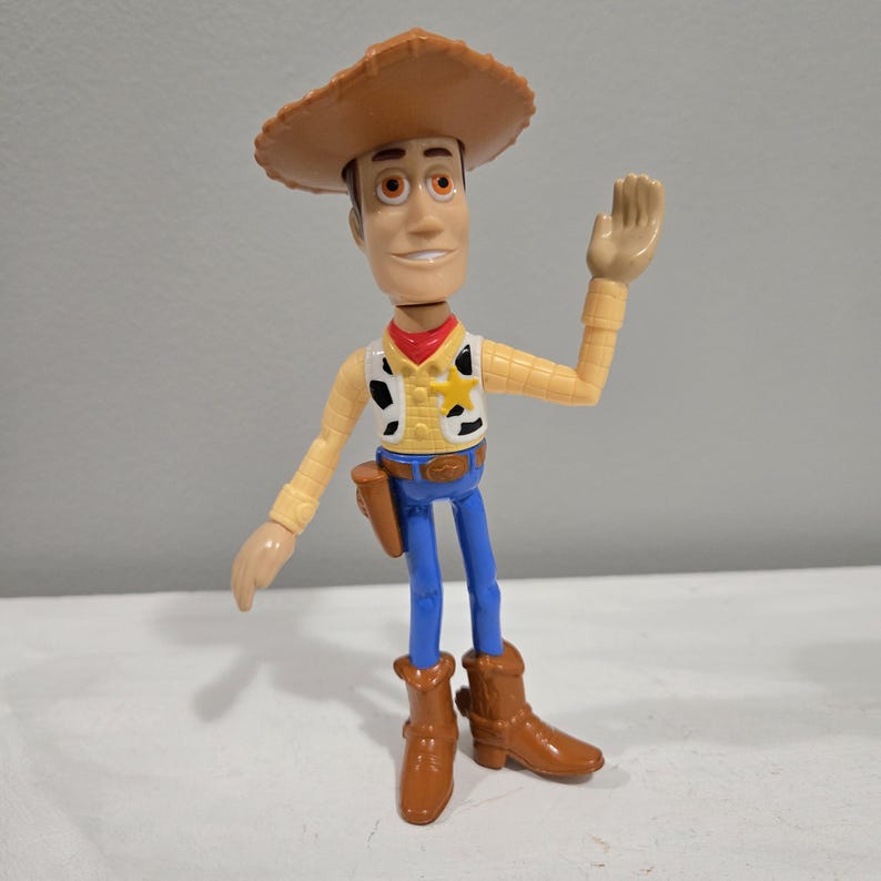 Pu&ograve; includere: Una figurina di plastica di Woody del franchise Toy Story. Woody indossa il suo cappello da cowboy marrone distintivo, una camicia gialla con una bandana rossa, un gilet blu con una stella da sceriffo, jeans blu e stivali marroni. Sta salutando con la mano destra.