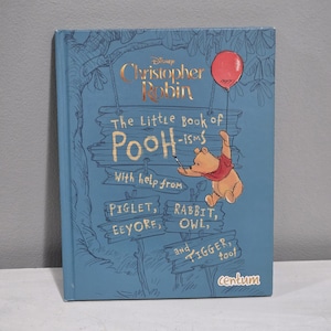 May include: A blue hardcover book titled "The Little Book of Pooh-isms" featuring Winnie the Pooh holding a balloon. The cover also includes the text "Christopher Robin" and the names of other characters.