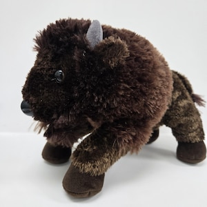 May include: A brown plush bison with a grey horn and black eyes. The bison is standing on all fours and has a shaggy coat.