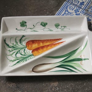 May include: White rectangular serving dish with two compartments, featuring hand-painted illustrations of carrots, green onions, and leafy green vines. The dish has a handle on each end.