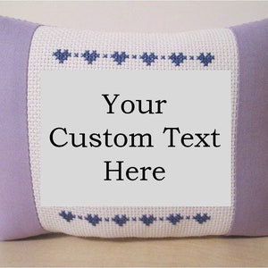 May include: A lavender pillow with a white embroidered panel featuring a row of blue hearts at the top and bottom. The panel has the text "Your Custom Text Here" in black.