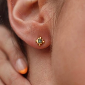 Puede incluir: Pendientes de botón de oro con una pequeña piedra preciosa cuadrada verde en el centro.