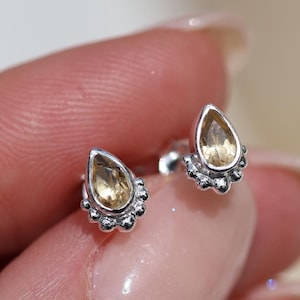Peut inclure: Une paire de boucles d'oreilles en argent en forme de goutte avec de petites pierres précieuses claires. Les boucles d'oreilles ont une bordure perlée autour de la pierre précieuse.